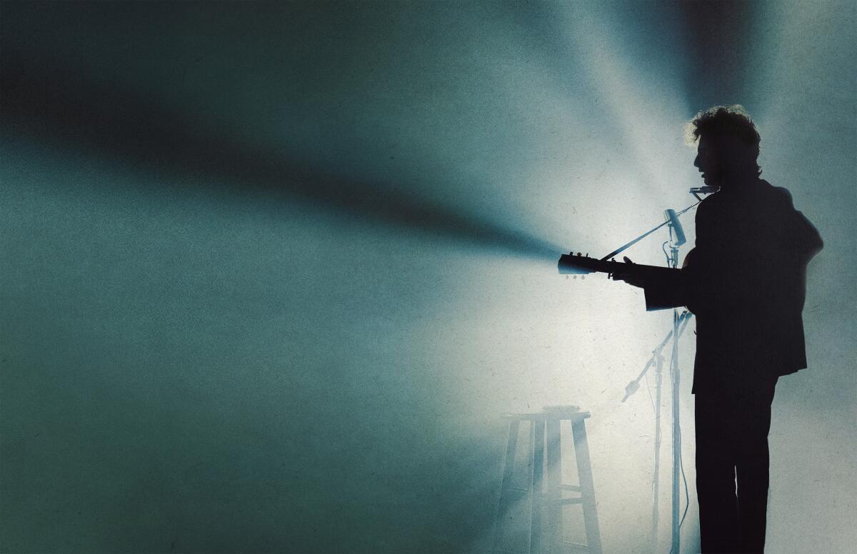 A man with a guitar stands in the spotlight.