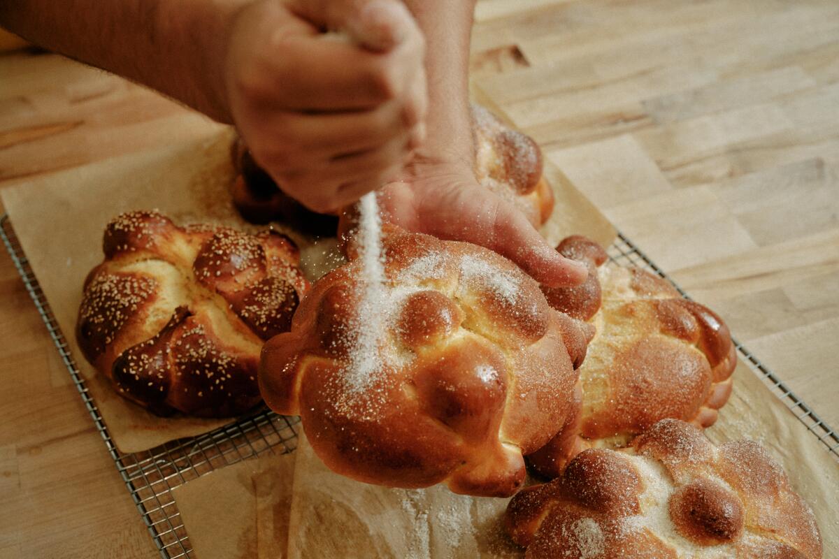 A hand drizzles sugar onto freshly baked pan de muerto