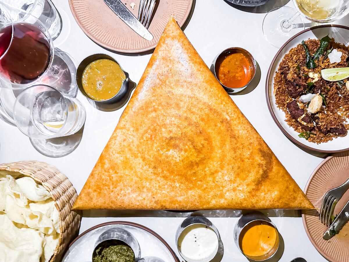 A triangular Mysore masala dosa surrounded by small metal cups of sauces and other dishes