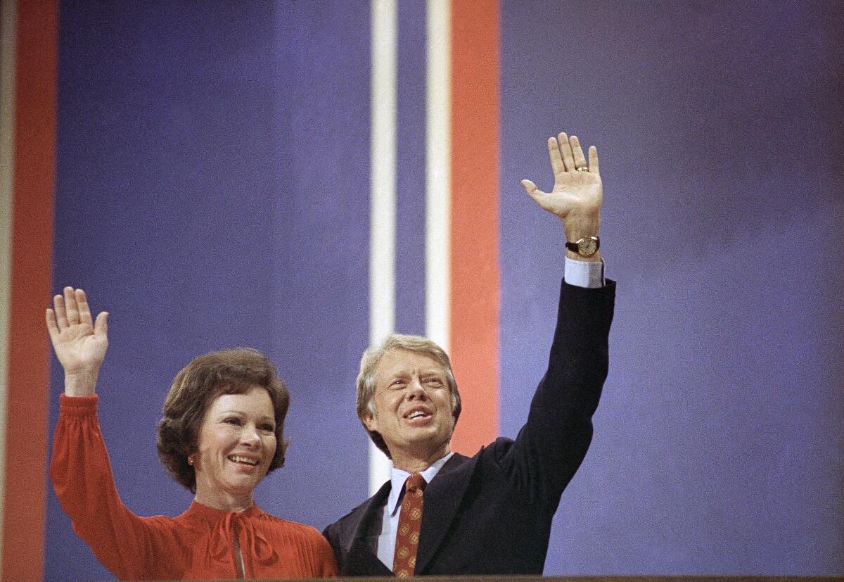 Jimmy and Rosalynn Carter against a blue political convention backdrop with red and white stripes, waving