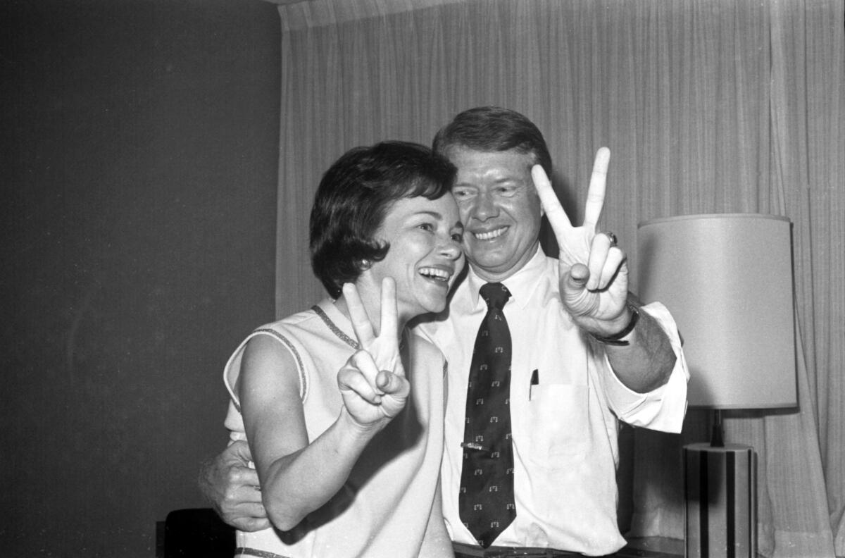 Rosalynn and Jimmy Carter smile and hold up their fingers in V shapes.