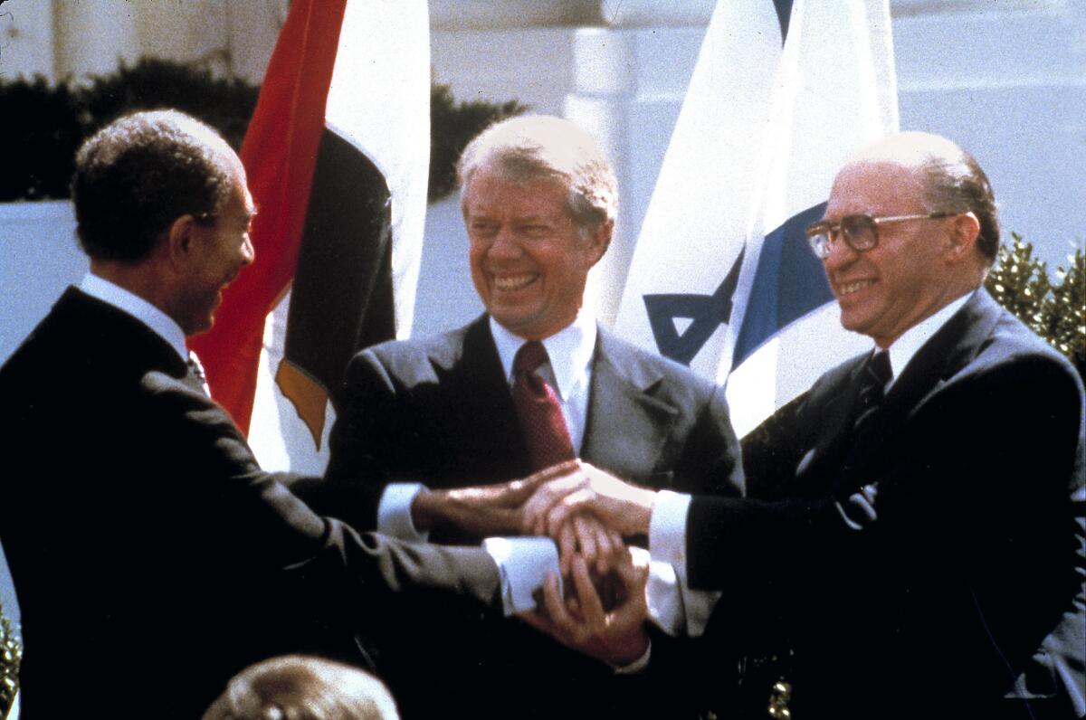 President Carter clasps hands and smiles with Anwar Sadat and Menachem Begin.