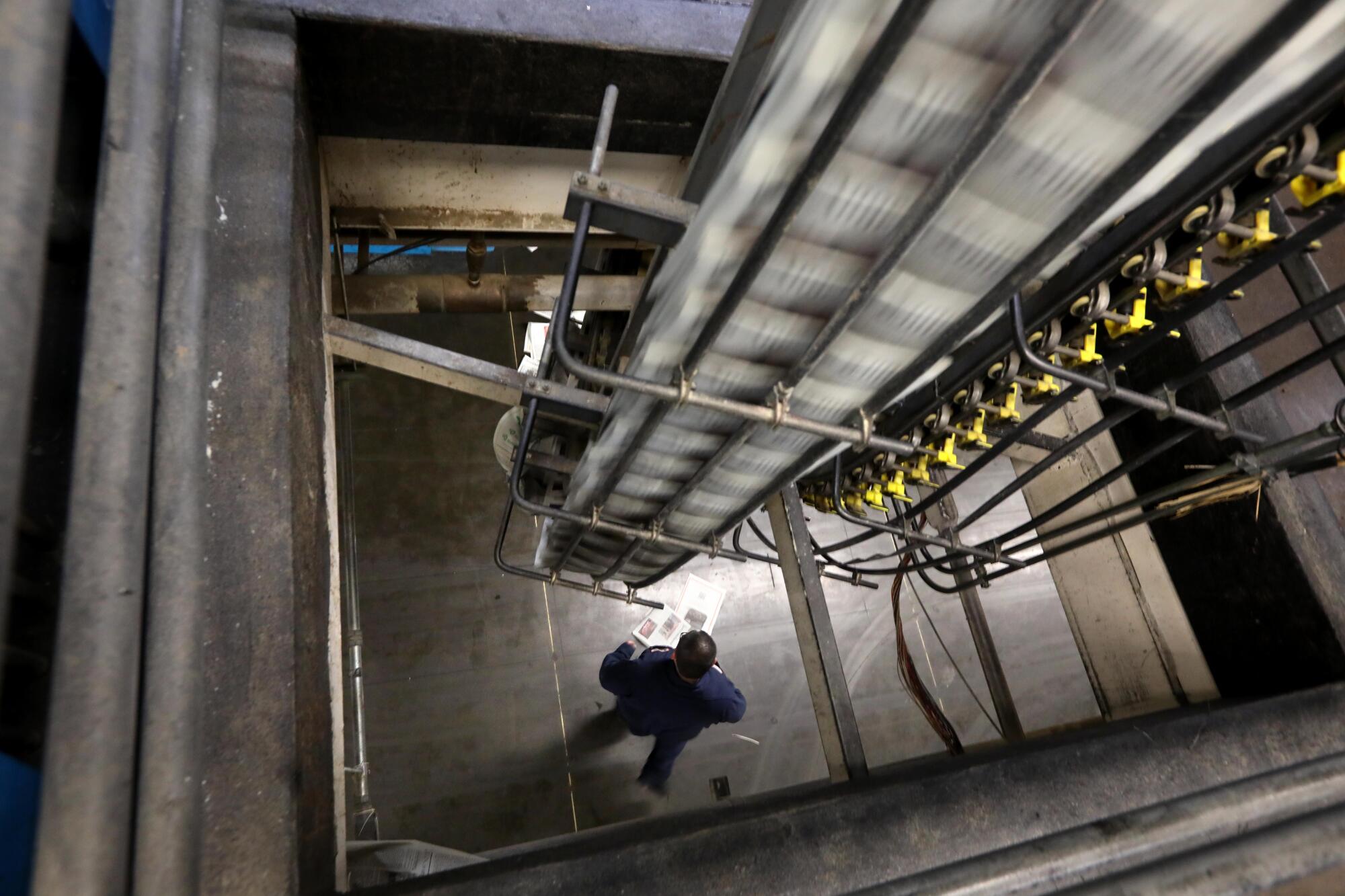 A pressman stands below a conveyor belt transporting stacks of the L.A. Times