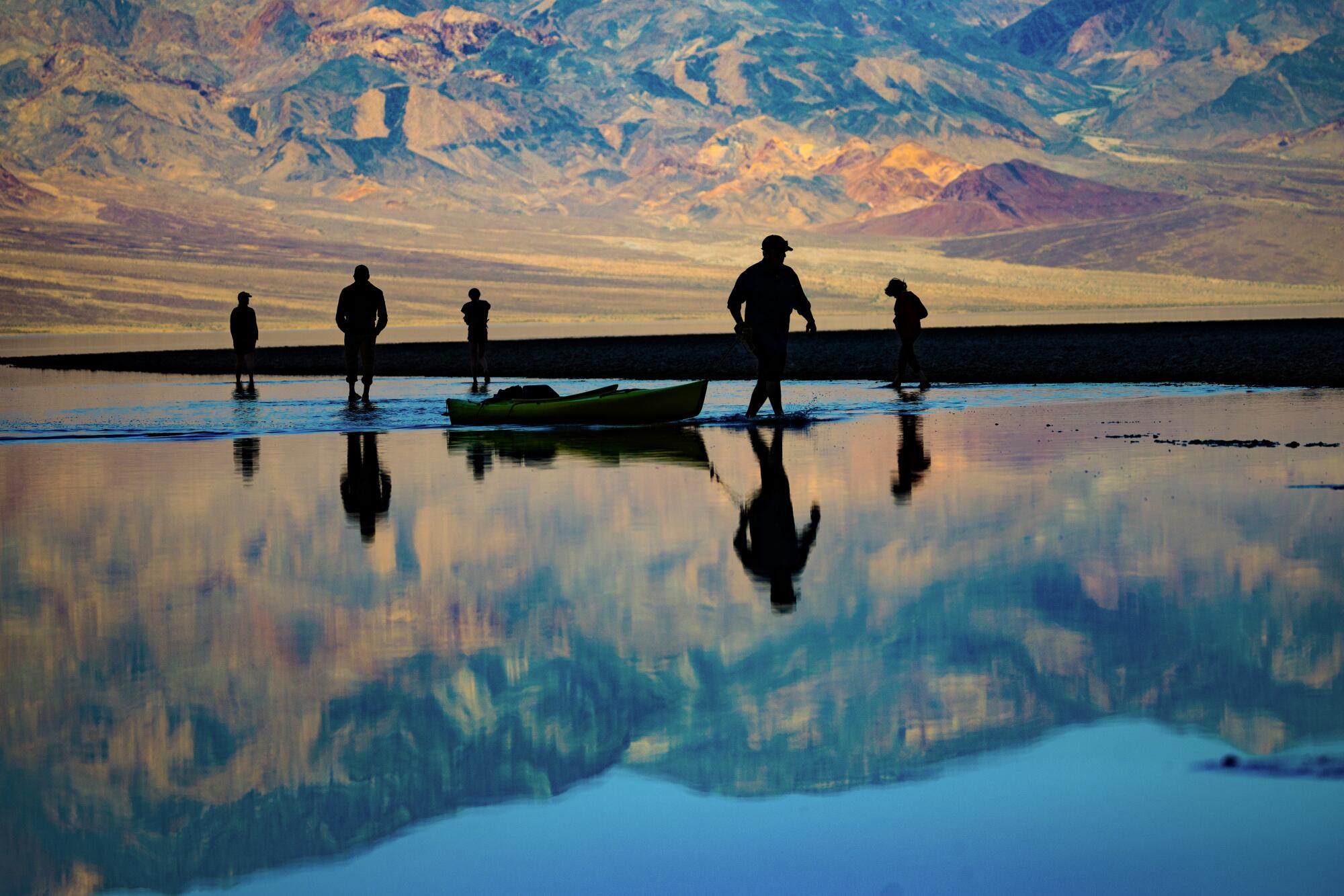 A lake reflects five people in silhouette against a mountain range