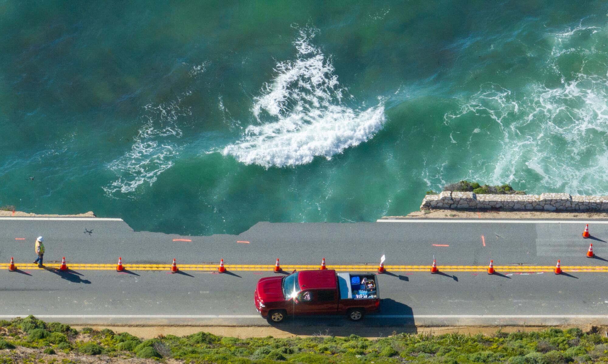 An aerial view of a truck near a broken section of highway, with the ocean beyond