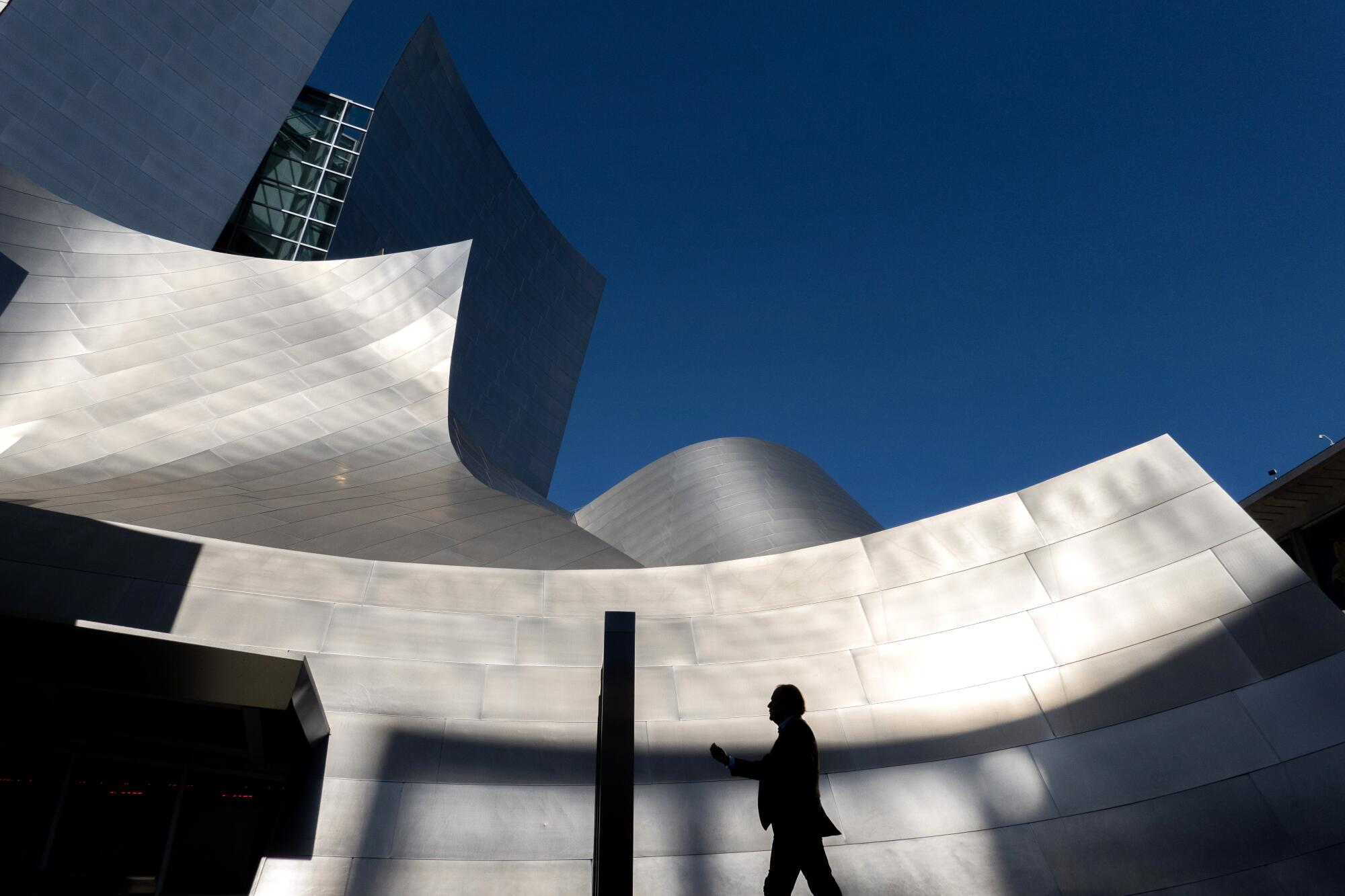 A pedestrian walks past Walt Disney Concert Hall on a sunny, spring morning.