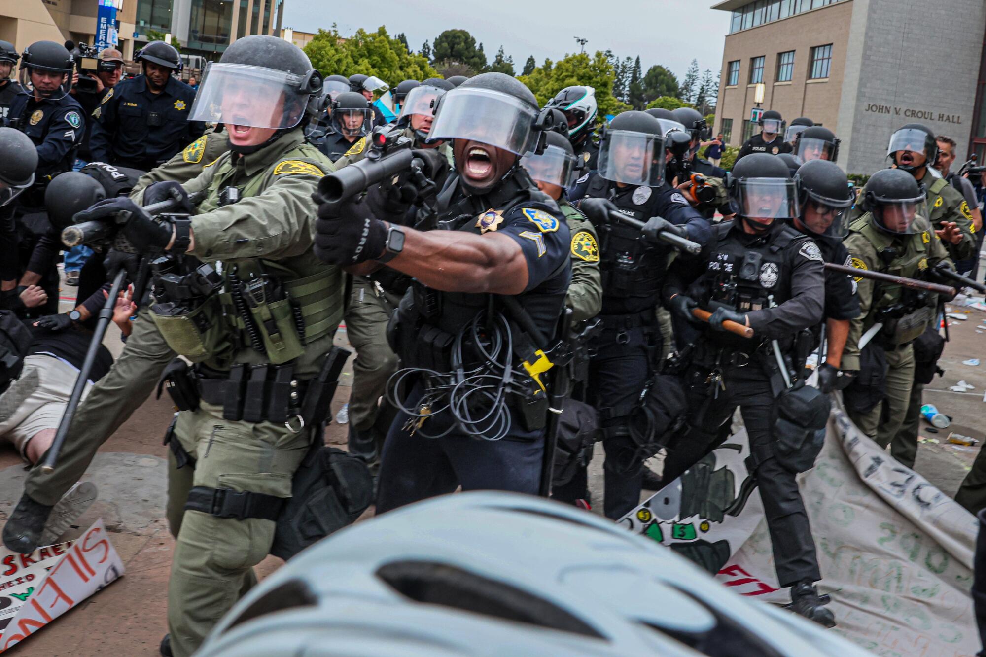 Law enforcement in riot gear hold batons and launchers during a campus demonstration