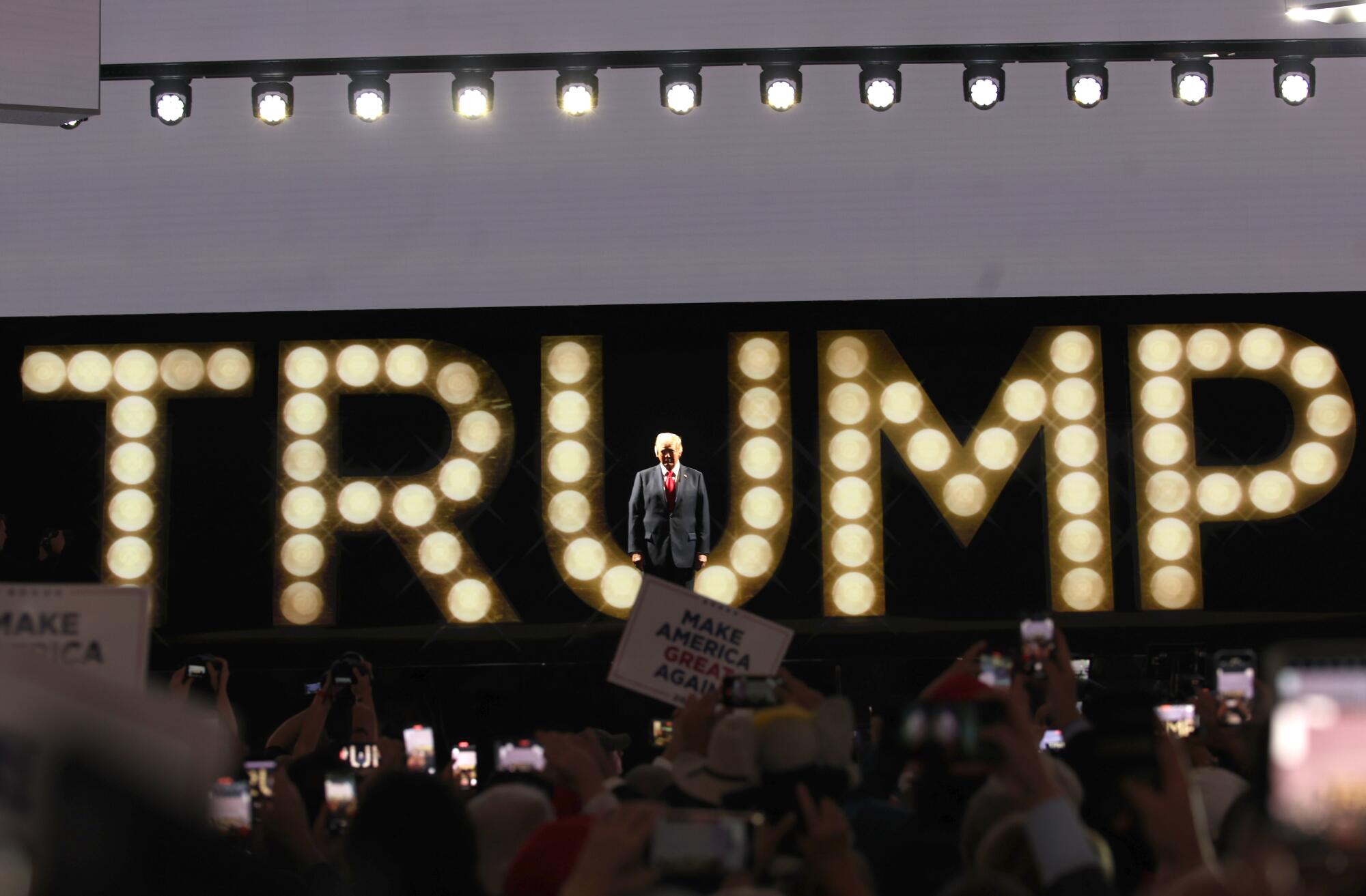 Donald Trump onstage with lightbulbs spelling his name in the background