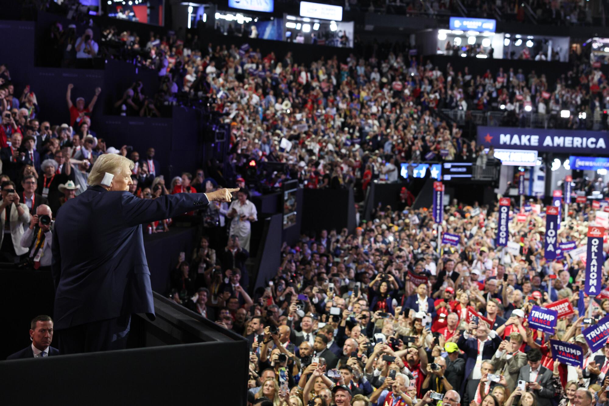 Donald Trump, right ear bandaged, points from the balcony of a crowded convention center