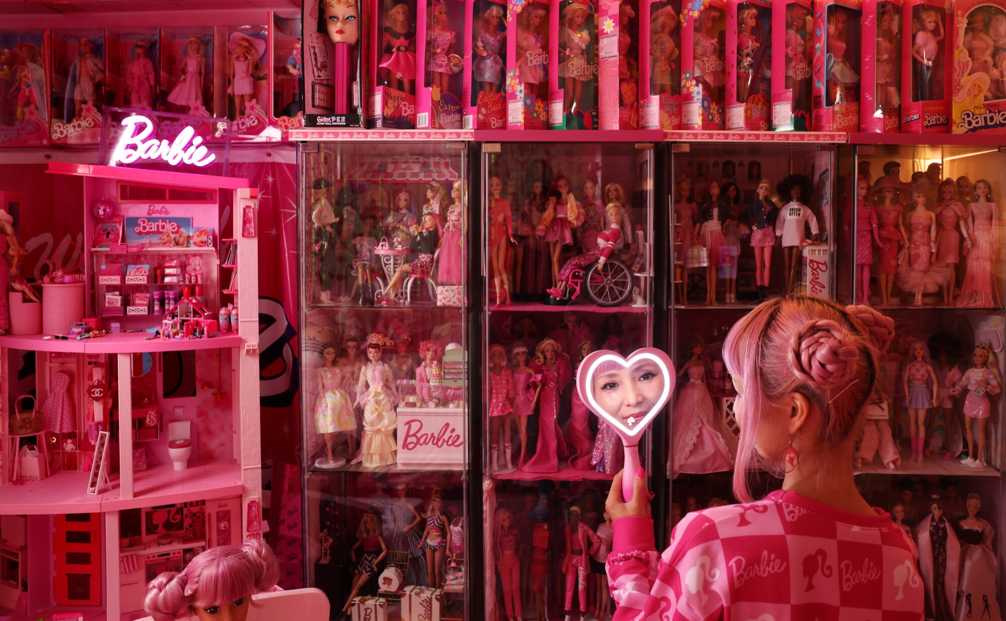 Barbie collector Azusa Sakamoto holds a heart-shaped mirror in a room full of pink merchandise