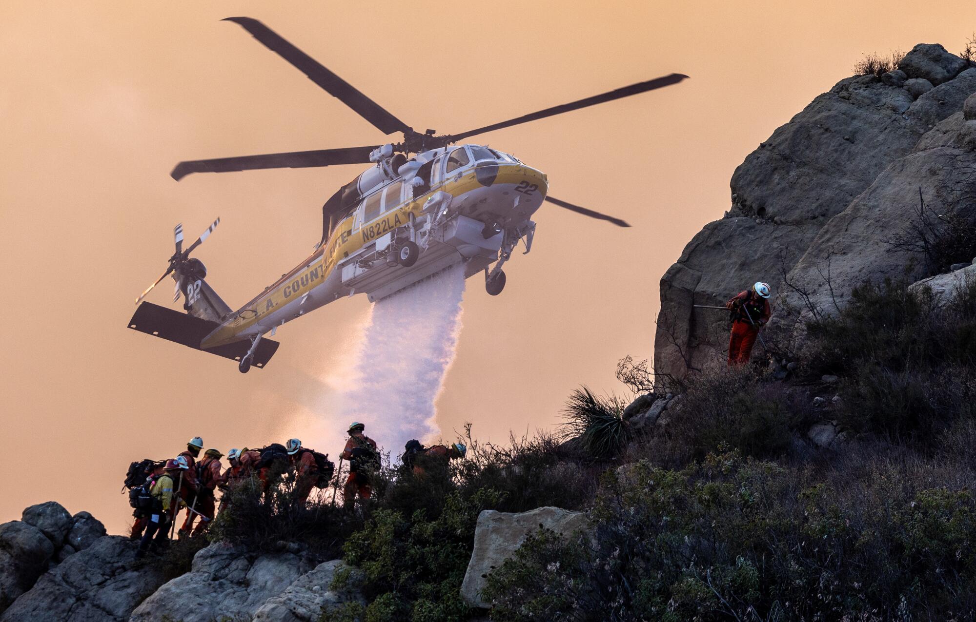 A fire crew ducks for cover on a ridge as a helicopter drops water in the distance