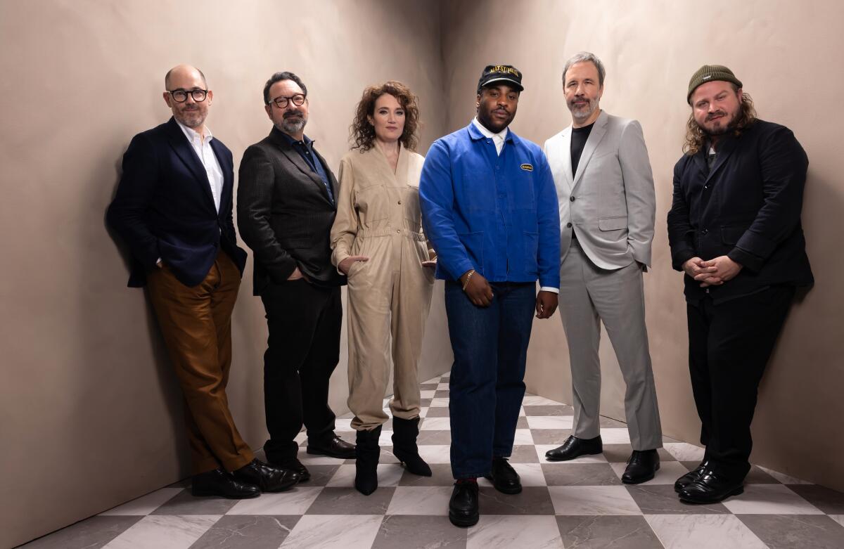 Six people stand on a checkerboard floor and pose for the camera.