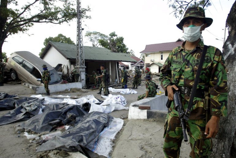 FILE - In this Friday, Dec. 31, 2004 file photo, an Indonesian soldier stands guard as his colleagues search for more bodies amidst the devastation at Banda Aceh, the capital of Aceh province in northwest Indonesia. The tsunami that struck on Dec. 26, 2004, was one of the world ' s worst natural disasters in modern times. It followed a magnitude 9.1 earthquake that ruptured the sea floor off Indonesia ' s Sumatra island, displacing billions of tons of water and sending waves 10 metres (33 feet) high radiating across the Indian Ocean at jetliner speeds. Associated Press journalists who covered the story recall some of the most poignant images from the disaster. (AP Photo/Bullit Marquez, File)