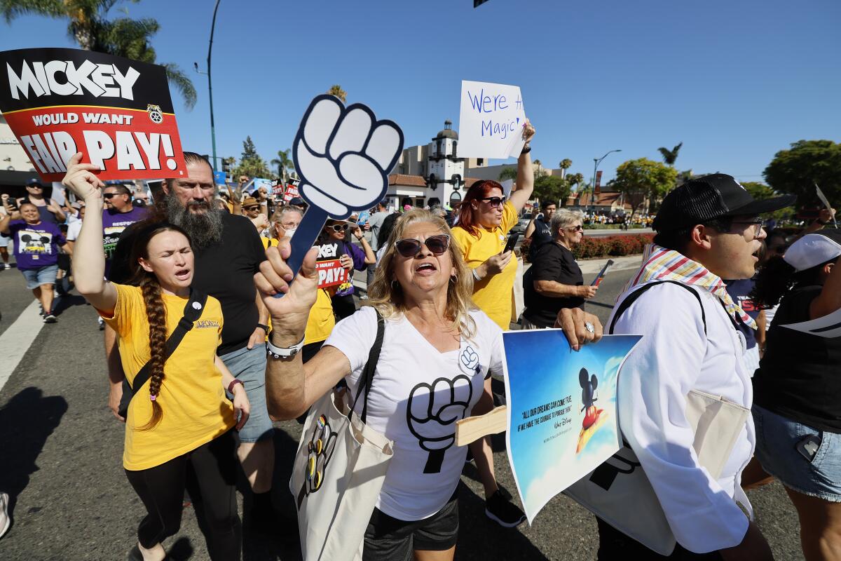 A group of workers marching down a street shouting and holding picket signs.