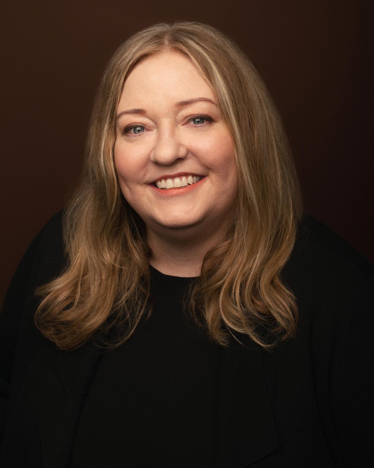 A portrait of a smiling woman with long brown hair in a black top.