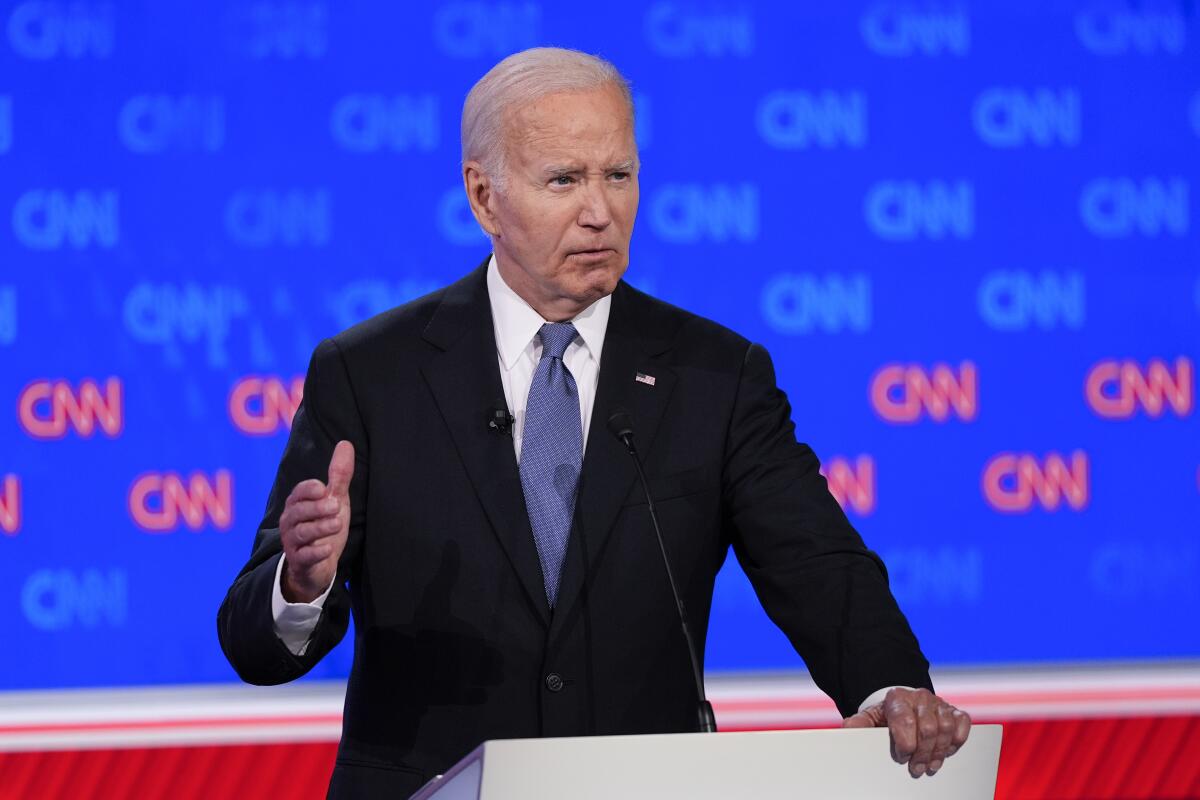 President Joe Biden speaks at a podium in front of a wall filled with CNN logos. 