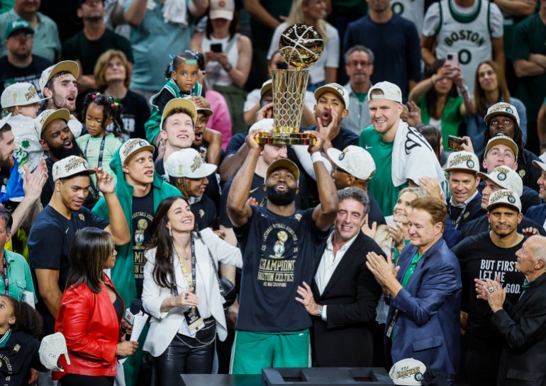 Boston Celtics player holds NBA Championship trophy.