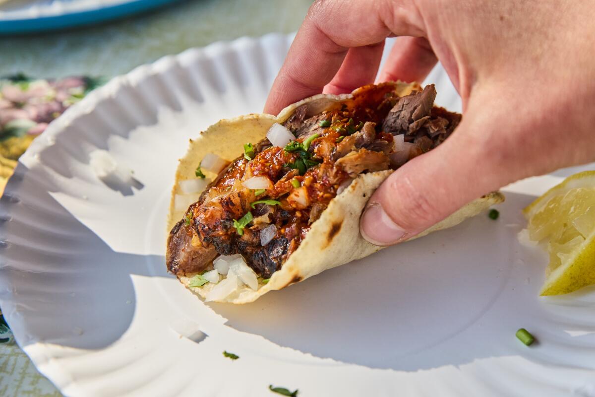 Moronga taco held by a hand while sitting on a plate.