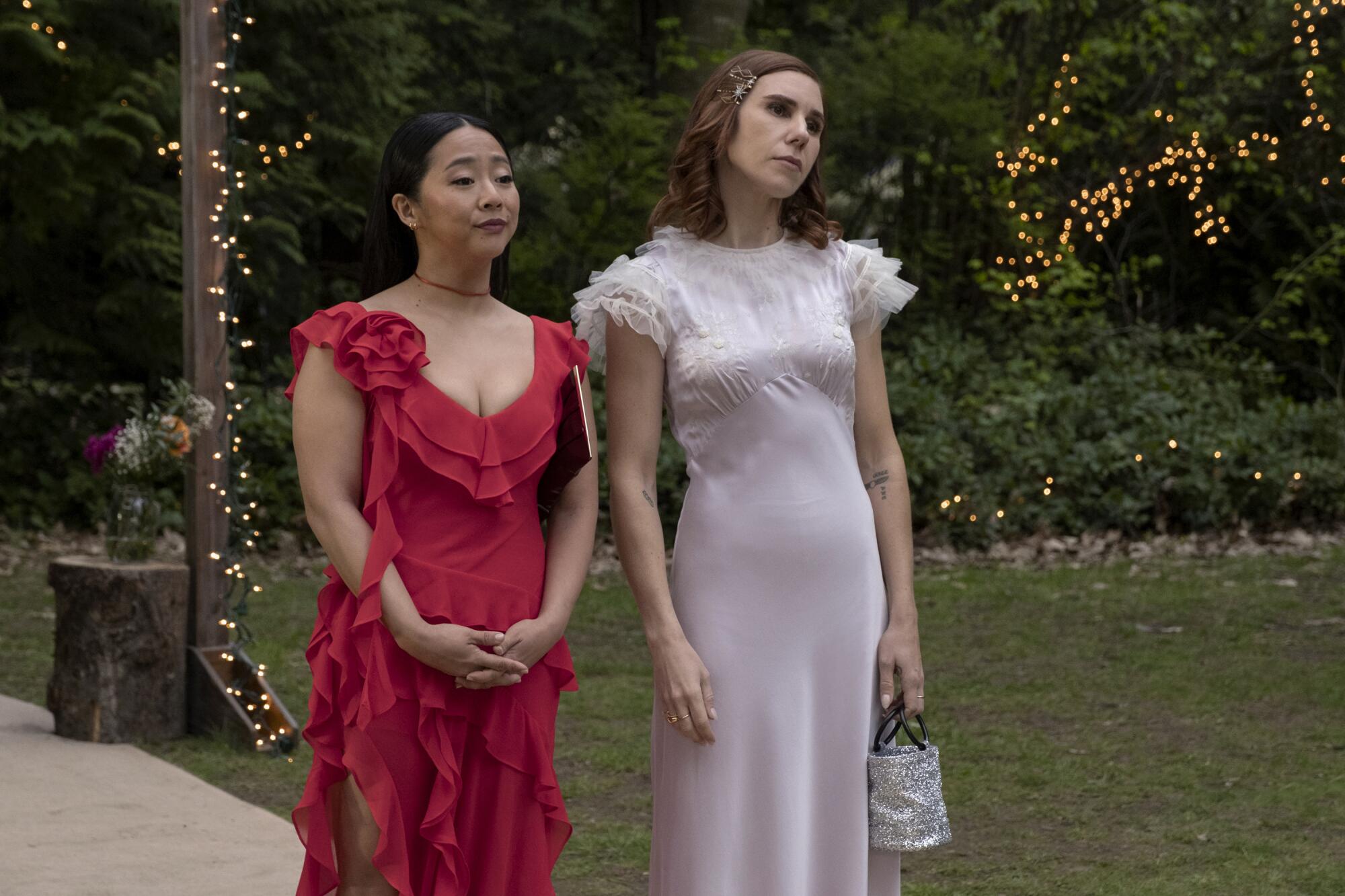 A woman in a red dress stand next to a woman in a white dress at an outdoor event.