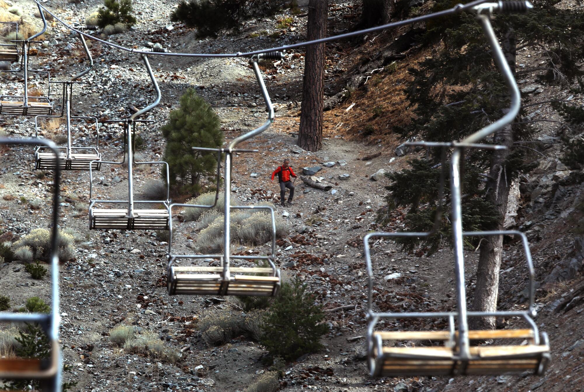 A hiker makes his way down a slope lined with ski lifts.  