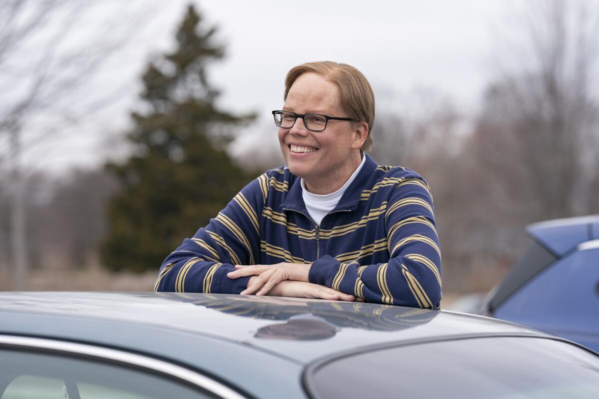 A man leans against a car, smiling