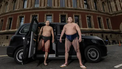 Getty Images Two sumo wrestlers standing outside a black cab in front of the Royal Albert Hall