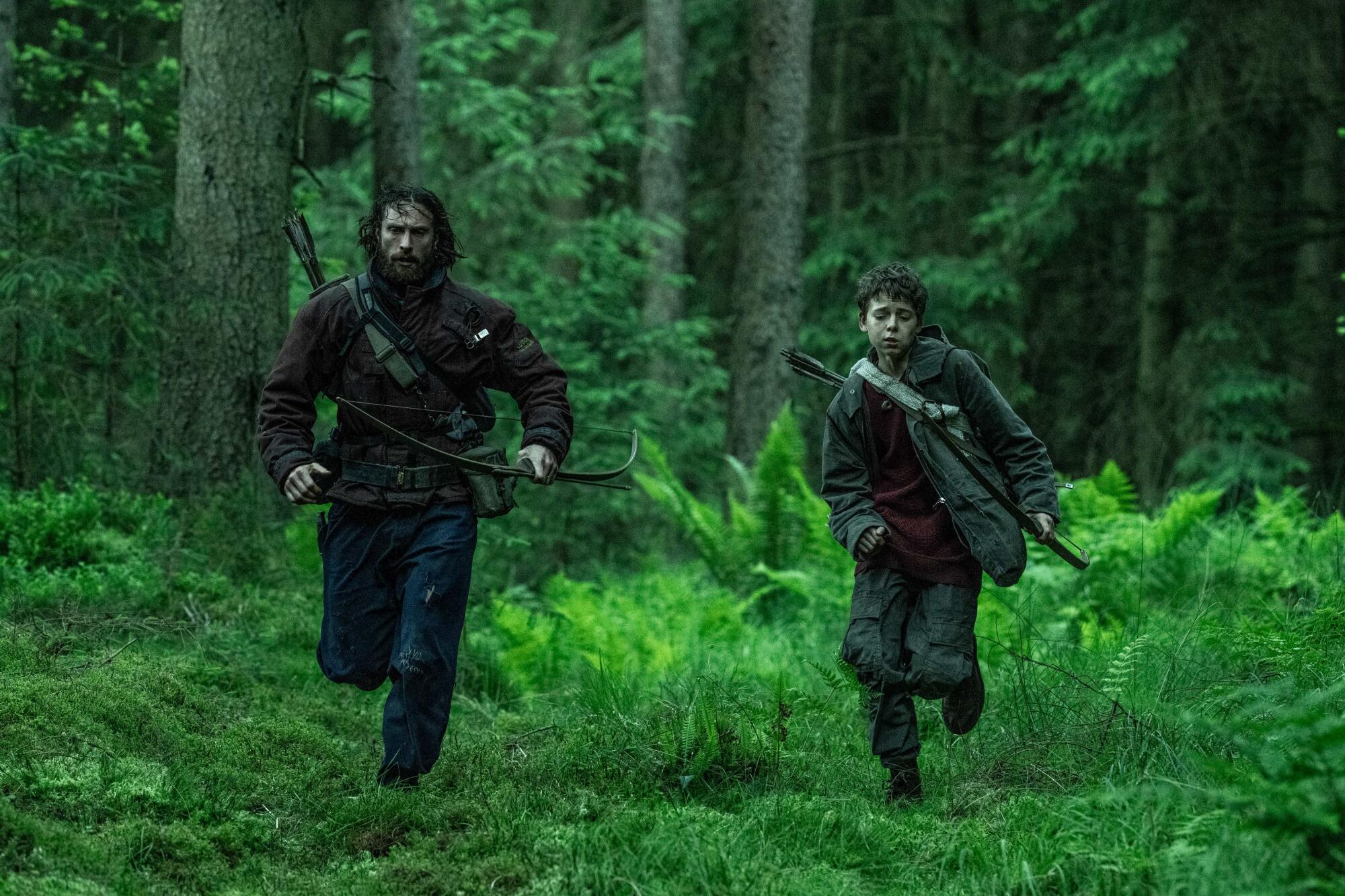 Two men run in the forest.