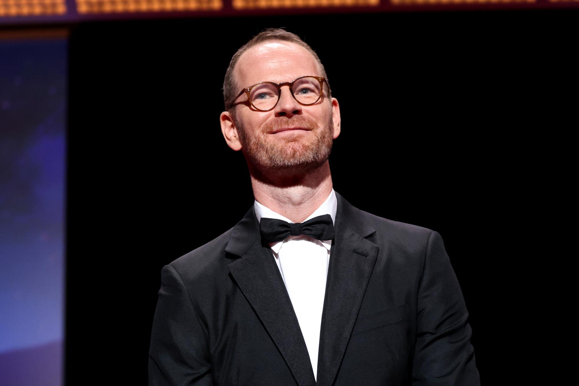 A man in a tuxedo smiles.