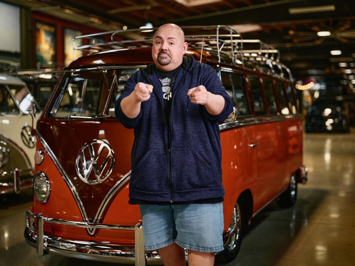 Gabriel Iglesias points fingers next to a vintage Volkswagen bus.