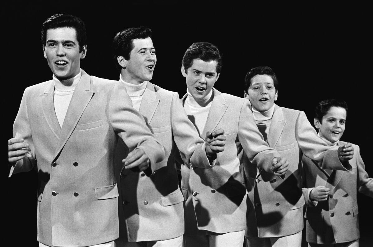 Five Osmond brothers of varying ages, arranged from tall to short, wearing suits in a black-and-white photo