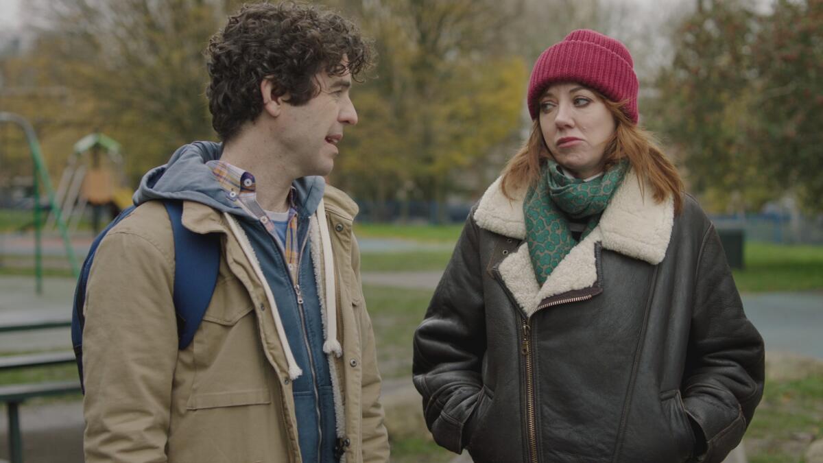 A man and a woman in winter jackets stand outside talking