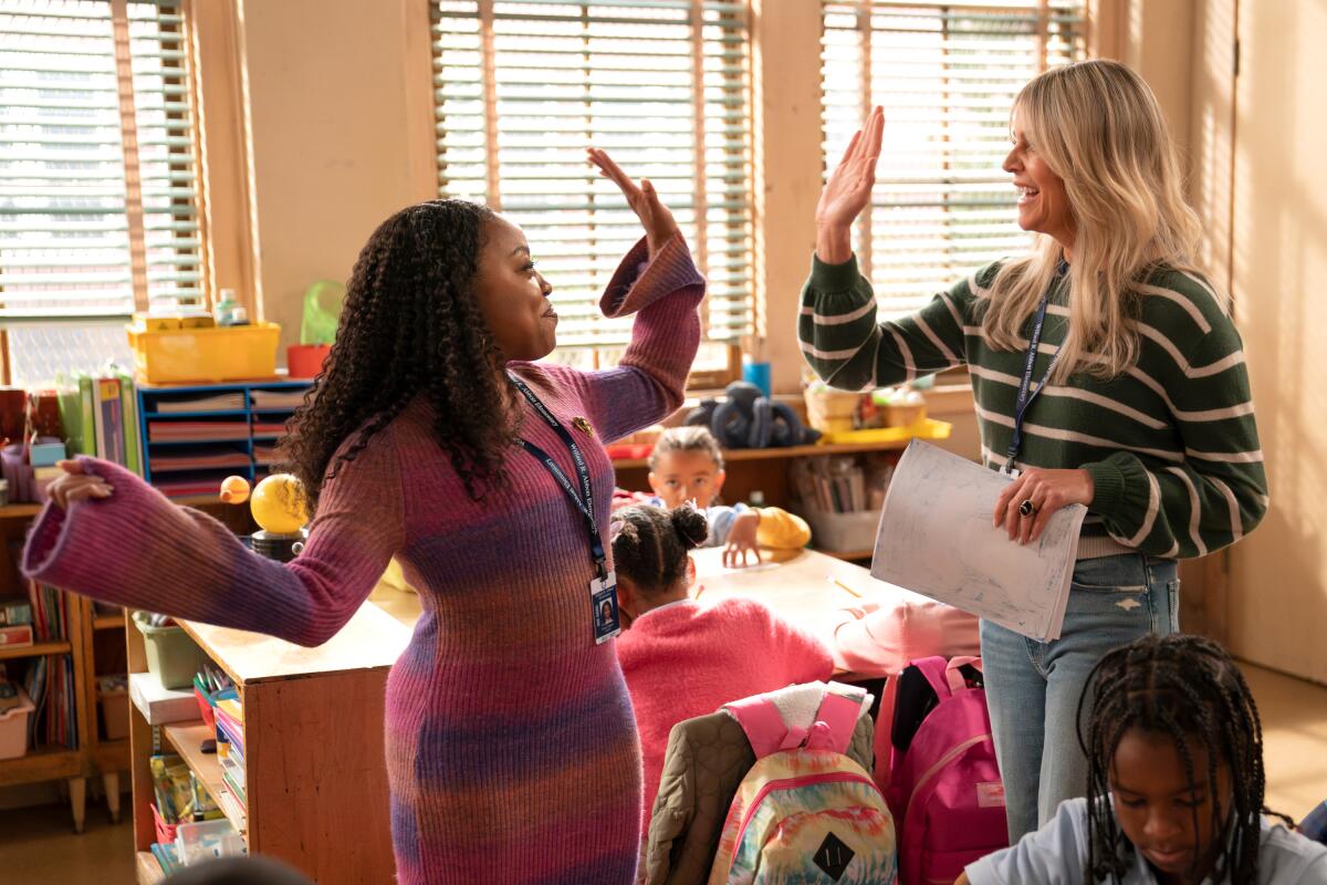 A woman in a pink and purple striped dress high-fives a blonde woman in a blue and white striped sweater and jeans.