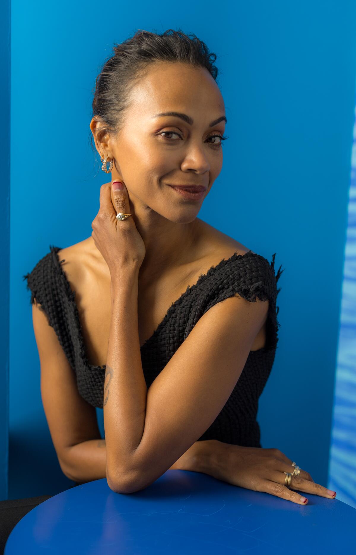 Zoe Saldaña poses for a portrait while sitting at a table.