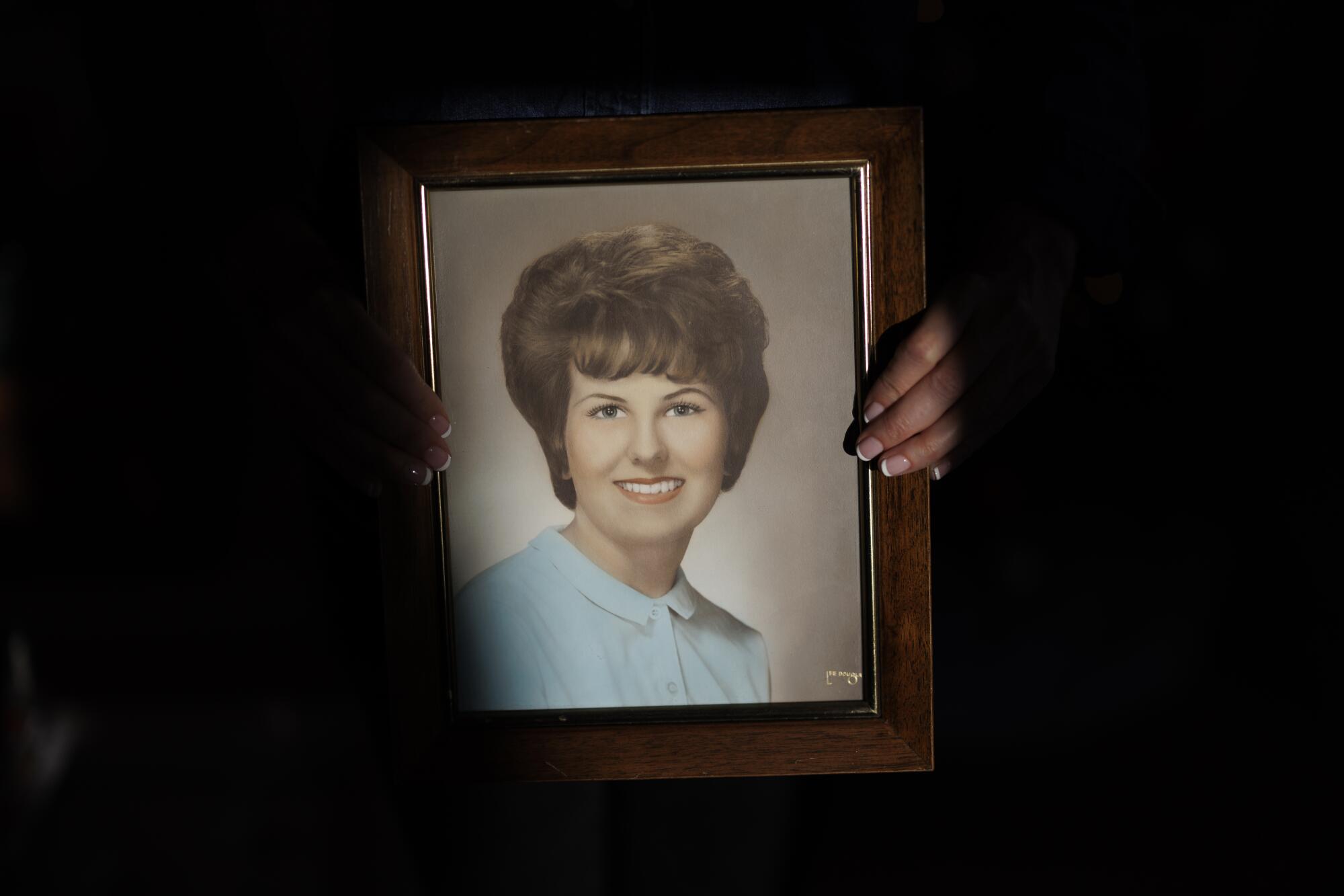 A framed portrait of a smiling woman with short, dark hair, wearing a pale blue top