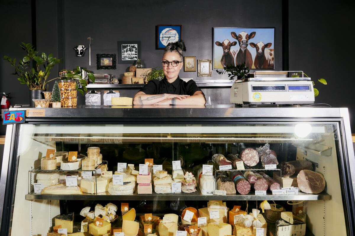 Lydia Clarke rests her arms on a display case of different cheeses and meats