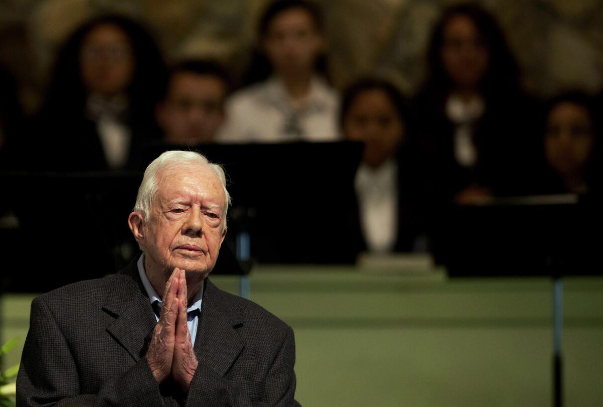 Former President Jimmy Carter pictured in 2015 in a church sitting with his hands pressed together.