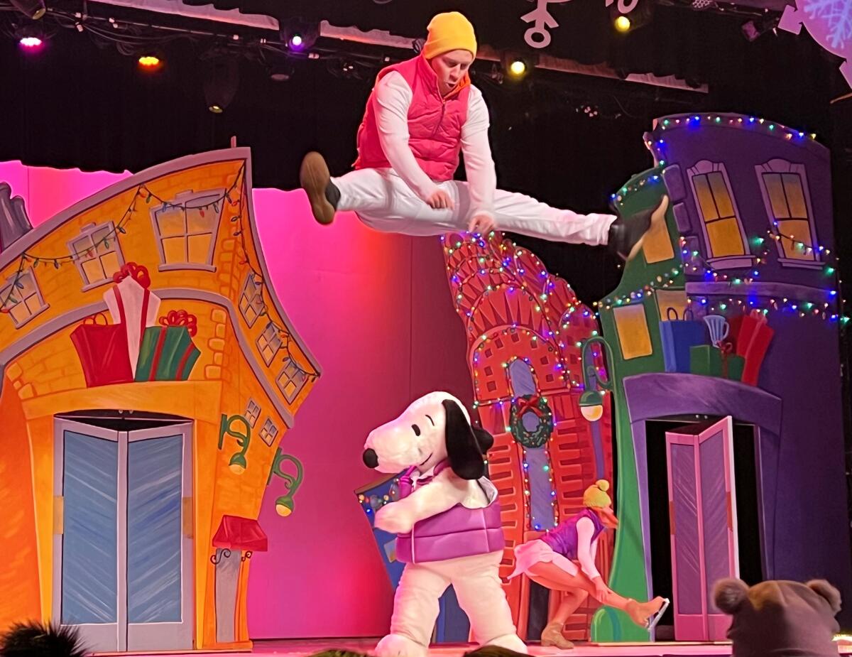 An acrobat, using a trampoline, jumps high as Snoopy and other performers ice skate below.