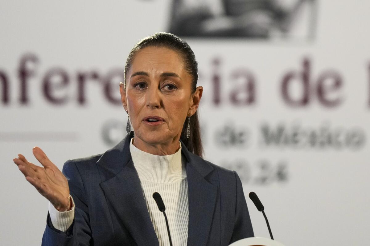 A woman gestures with one hand as she speaks into two small microphones.