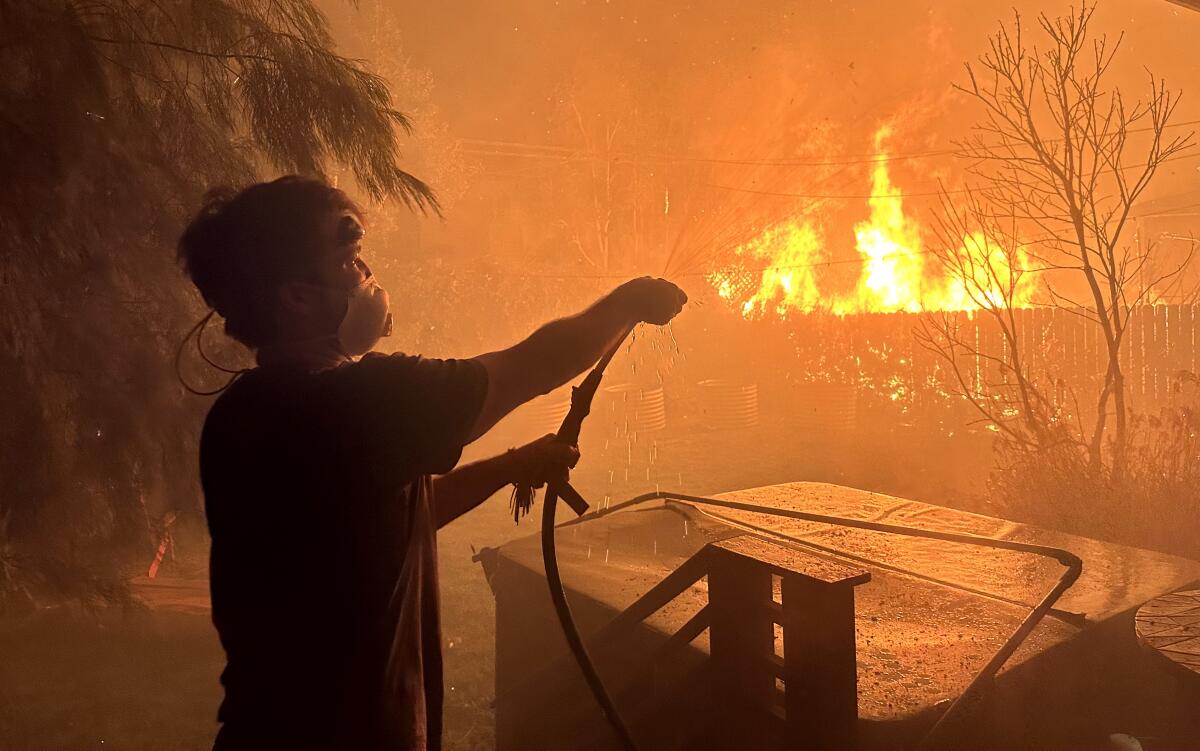 Orly Israel uses a garden hose to try to douse flames from the Palisades fire on Tuesday.