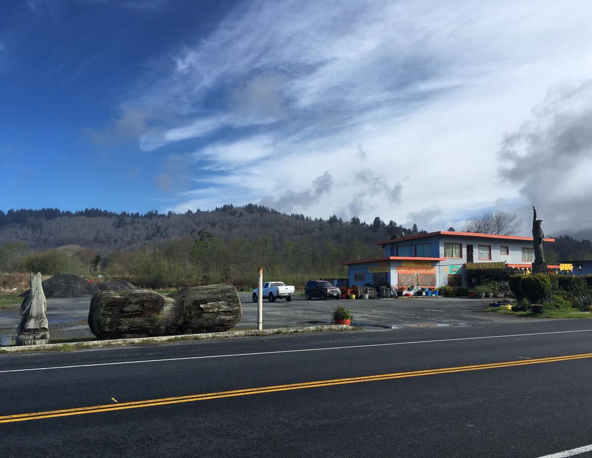 A large peanut carved from a redwood tree sits in a market parking lot alongside a highway.