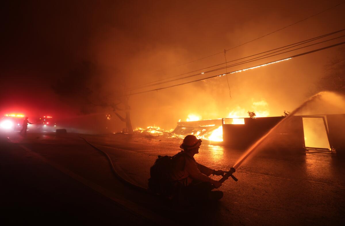 A firefighter battles a house fire as the Palisades Fire burns in Malibu Tuesday.