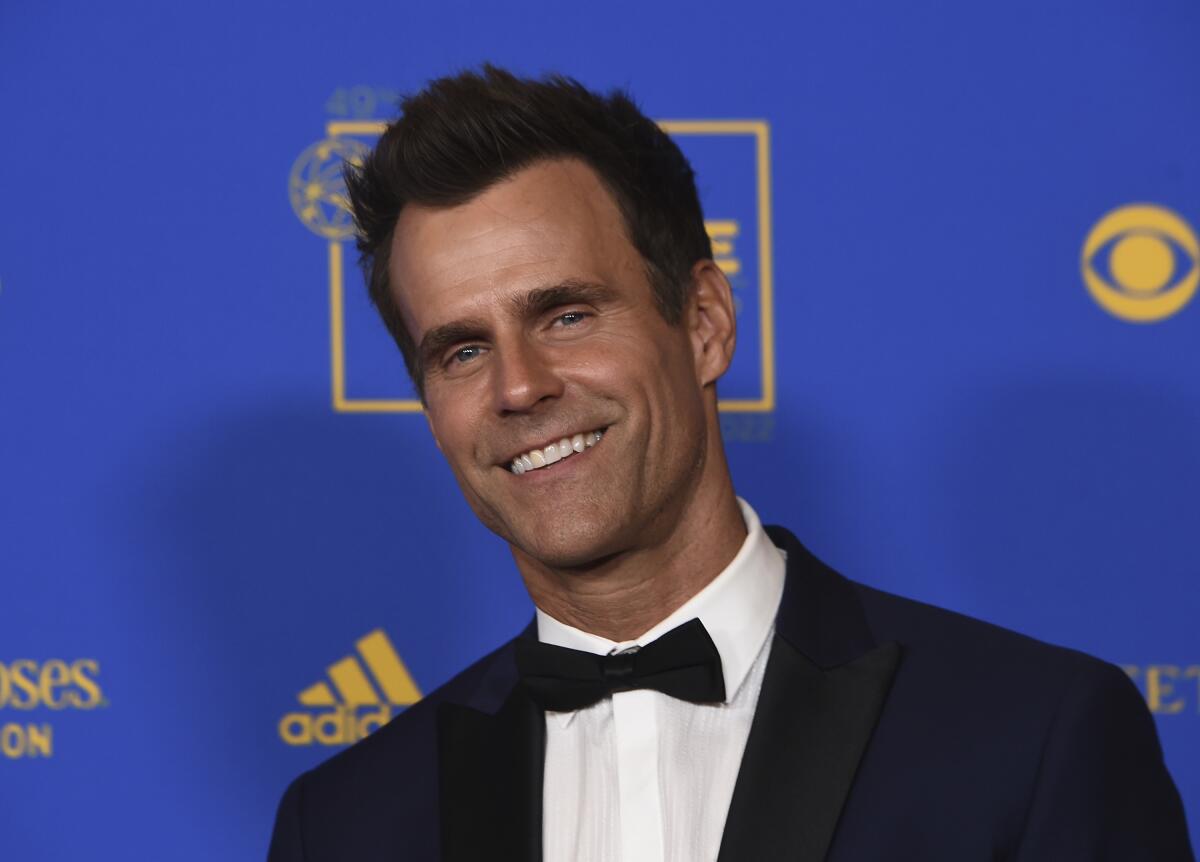 Cameron Mathison smiles in front of a blue backdrop