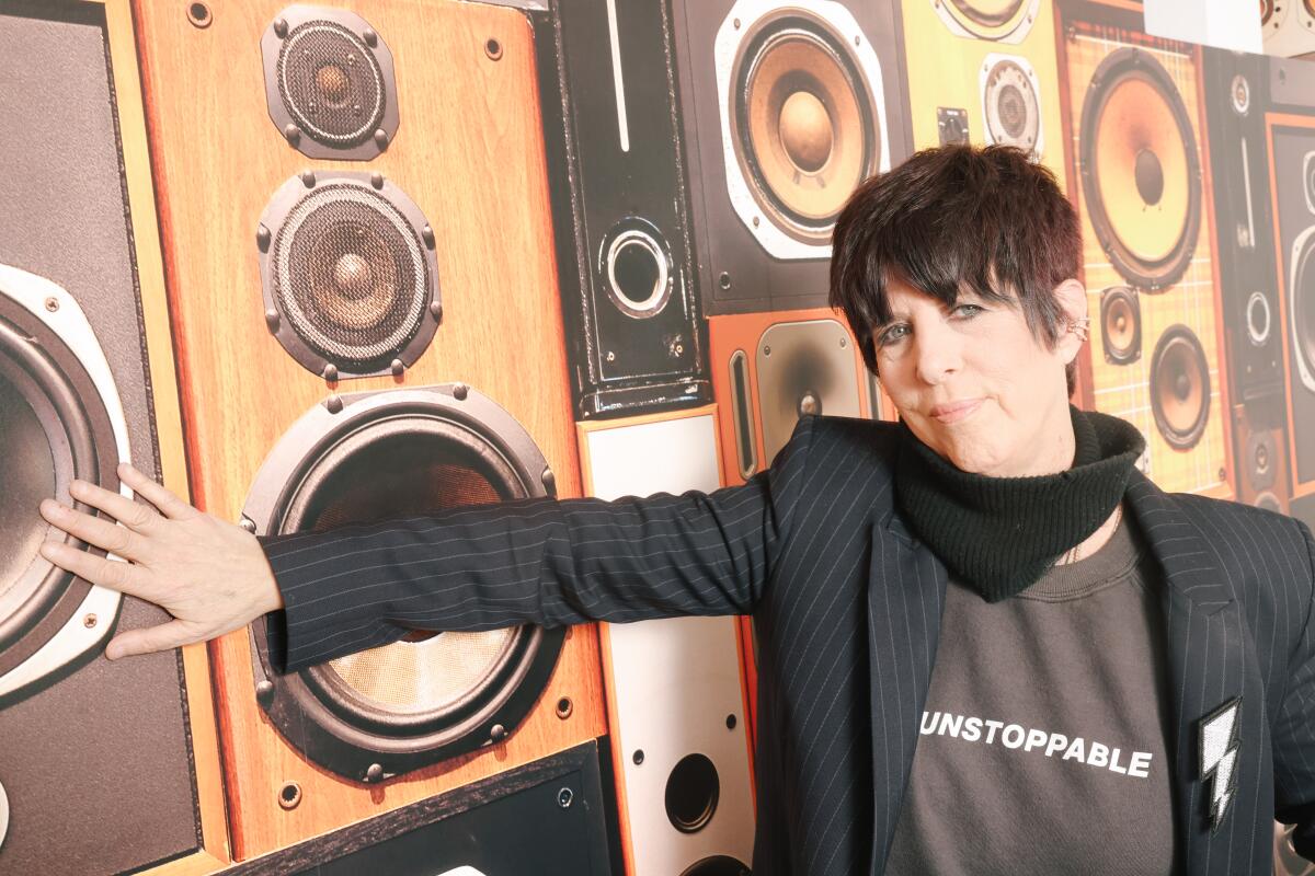 Songwriter Diane Warren leans against a wall showing speakers