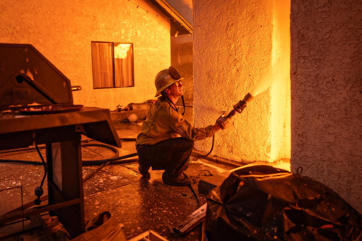 A firefighter sprays water from a hose into a burning house.