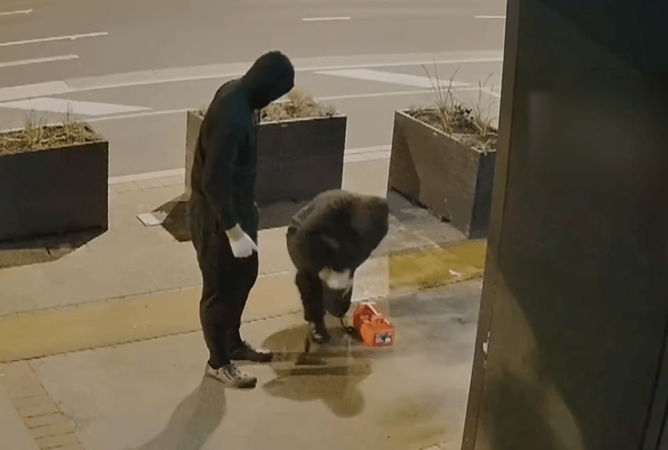 Two hooded figures placing an orange box on the ground.