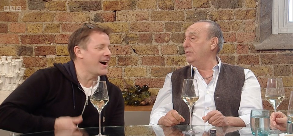 Two men sitting at a table, drinking wine and talking.