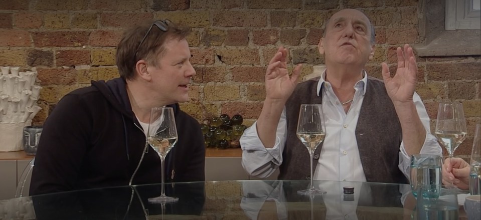 Two men sitting at a table, talking and drinking wine.