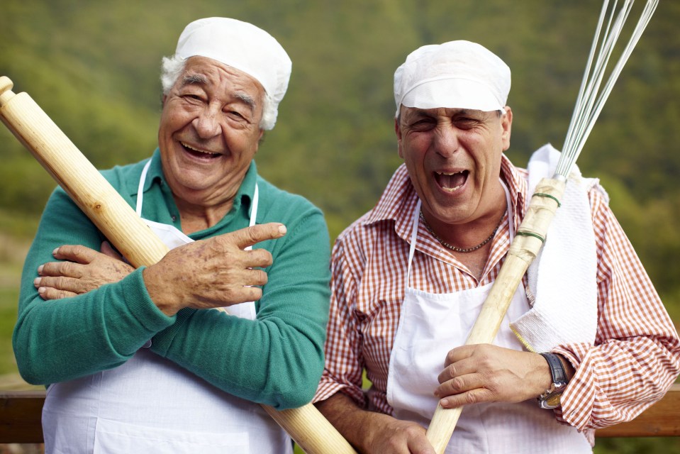 Two chefs smiling and holding kitchen utensils.