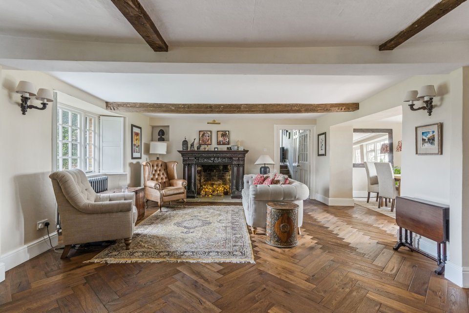 Living room of a manor house with herringbone floors, a fireplace, and antique furniture.