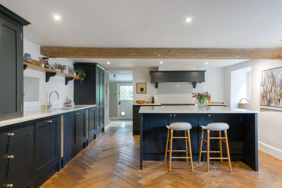 Kitchen of a £2.5m manor house with dark cabinetry, herringbone flooring, and an island.